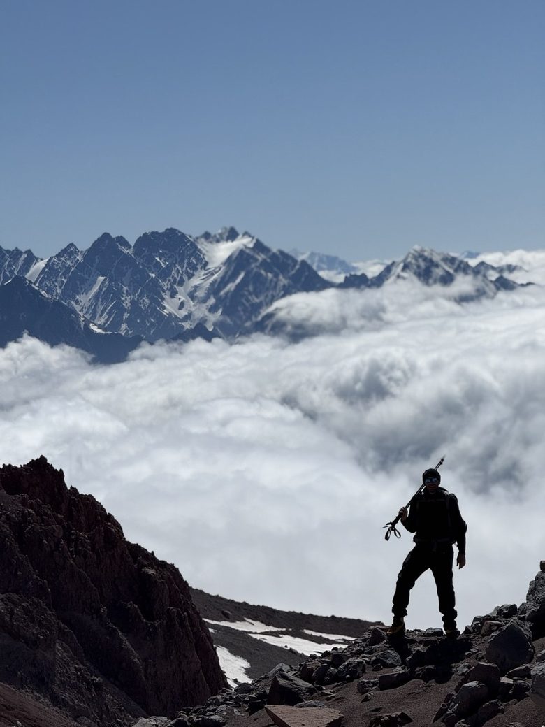 Standing above the cloud line on a mountain ridge with an ice axe